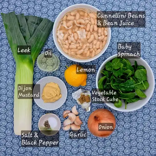   The labelled ingredients used in the Leeky Beans recipe. Leek, onion, oil, salt and black pepper, vegetable stock cube, garlic, cannellini beans and their bean juice, Dijon mustard, lemon and spinach. 