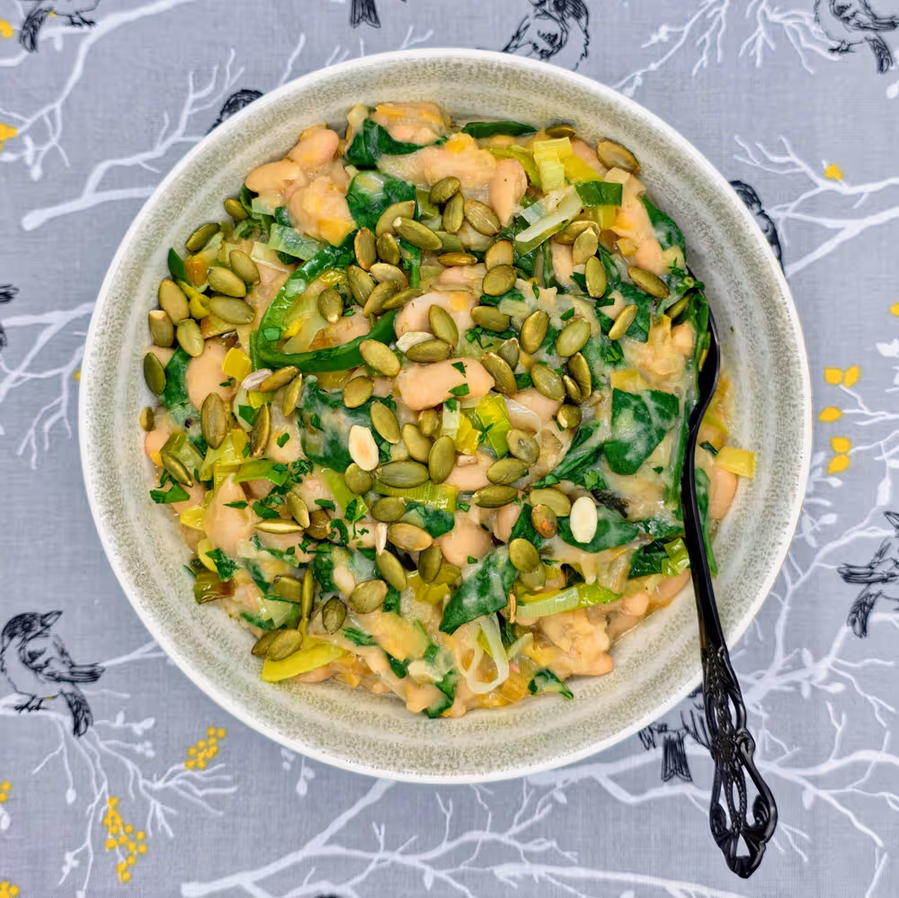  Leeky Beans plated in a bowl and topped with a sprinkle of toasted pumpkin seeds. 