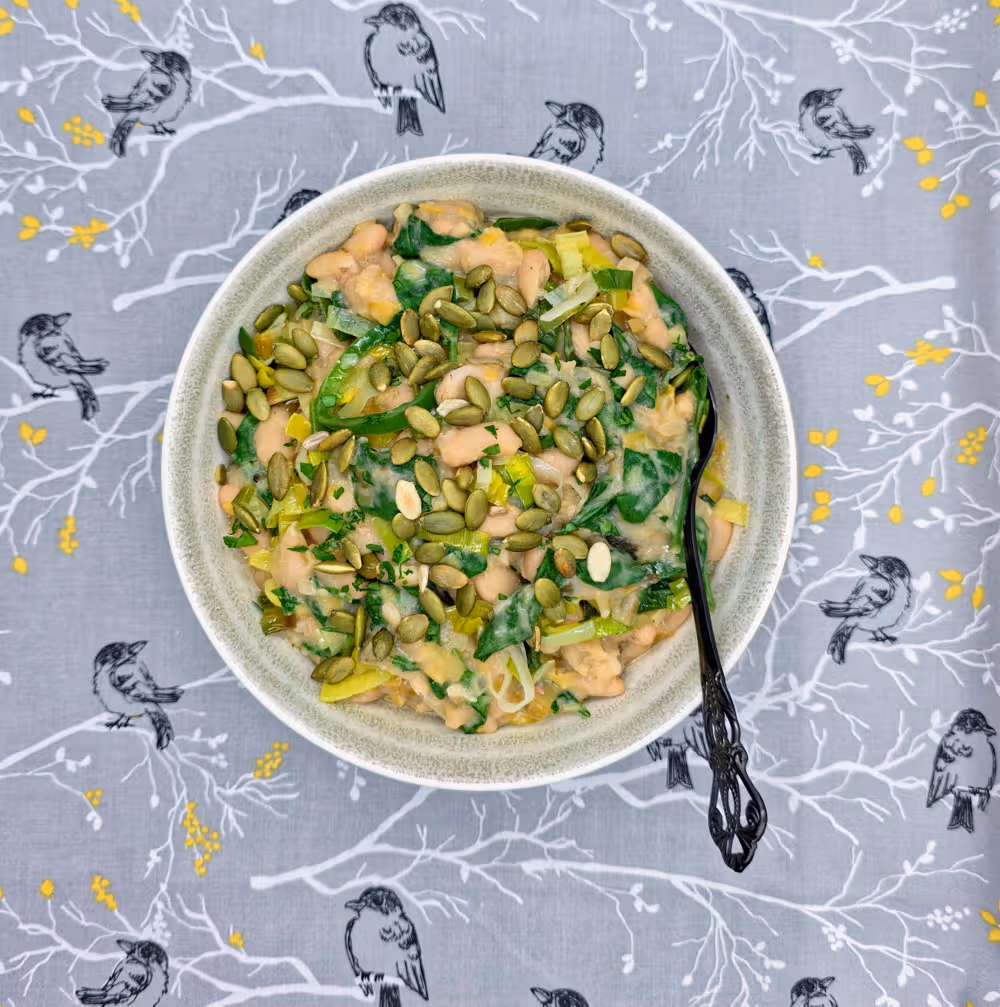  Leeky Beans plated in a bowl and topped with a sprinkle of toasted pumpkin seeds. 