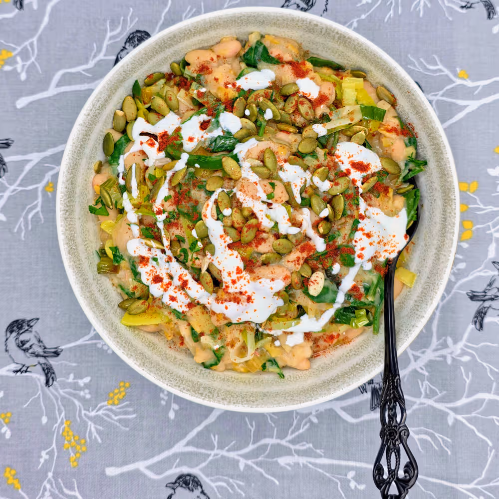  Leeky Beans plated in a bowl and topped with a sprinkle of toasted pumpkin seeds, a drizzle of Greek yoghurt and a sprinkle of smoked paprika. 